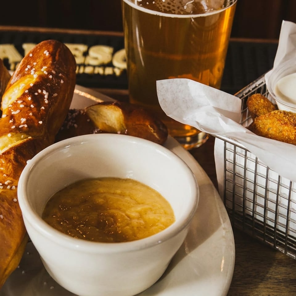 Soft pretzels with cheese dip, fried snacks with ranch dressing, and a pint of beer on a restaurant table.